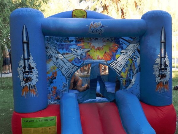 Un castello gonfiabile blu con decorazioni spaziali, bambini giocano all'interno.
