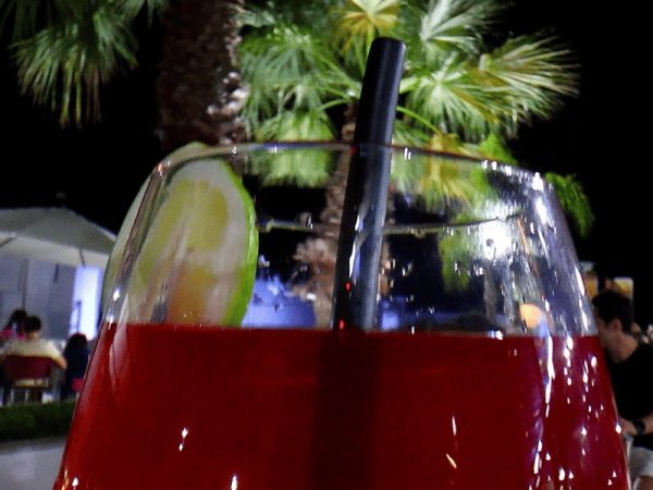 Bicchiere con bevanda rossa e fetta di lime, sfondo di palme notturne.
