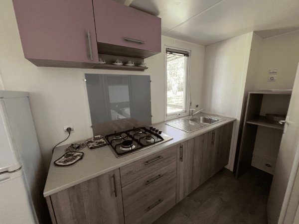 Cucina con piano cottura, lavello, pensili e frigorifero, finestra luminosa.