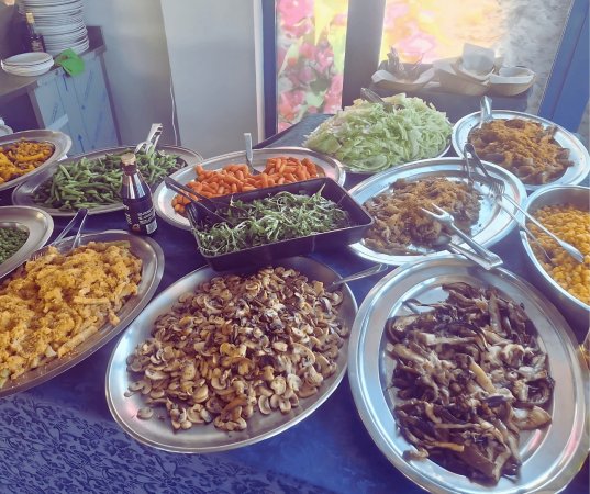 Un buffet con vari piatti di verdure e funghi su vassoi d'acciaio.