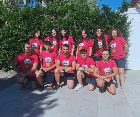 Un gruppo di persone posa sorridente indossando magliette rosa davanti a una siepe verde.