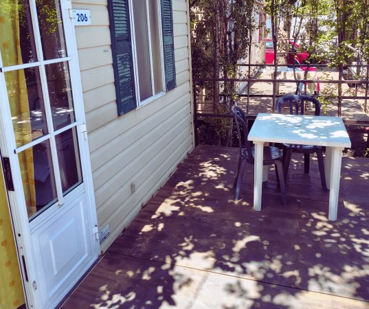 Una veranda con tavolo bianco e sedie di plastica, accanto a una casa mobile color crema.