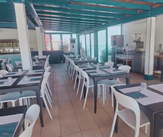 Sala da pranzo con tavoli e sedie bianche, soffitto e travi turchesi.