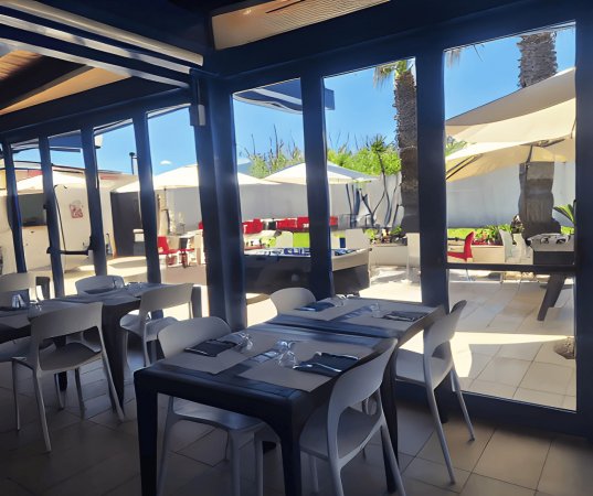 Ristorante con tavoli apparecchiati, vista su terrazza esterna con ombrelloni.