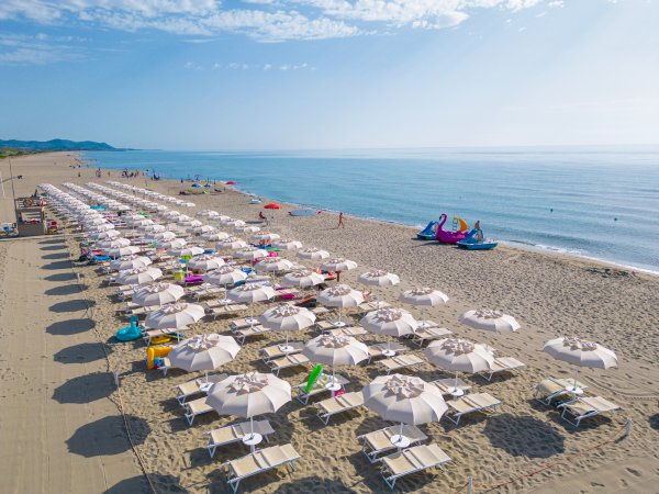 Spiaggia con file di ombrelloni bianchi e mare calmo.
