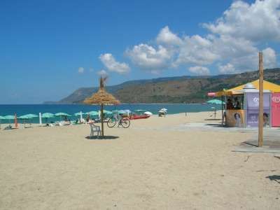 Spiaggia sabbiosa con ombrelloni verdi, capanni, bici e mare azzurro.