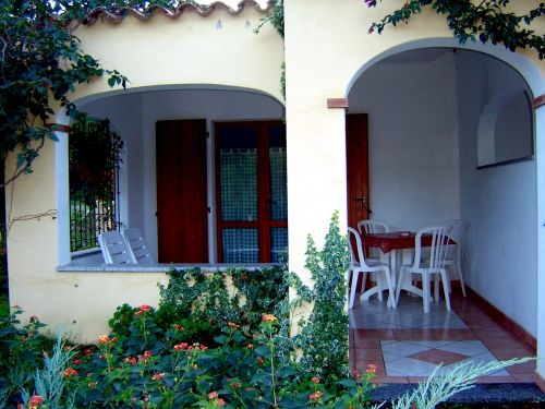 Tavolo e sedie bianche sotto un portico con verde rampicante.