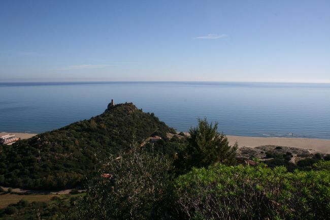 Vista panoramica di una collina verde che si affaccia su una vasta spiaggia e mare calmo.
