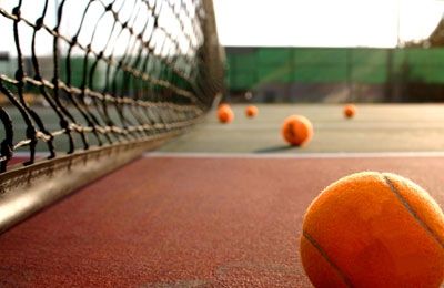 Un campo da tennis con palline arancioni sparse vicino alla rete.