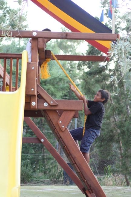 Bambino arrampica su una struttura da gioco in legno con una corda.