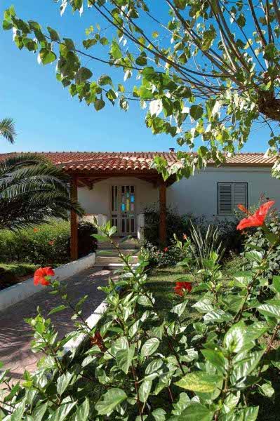 Giardino fiorito con una villa bianca e tetto rosso.