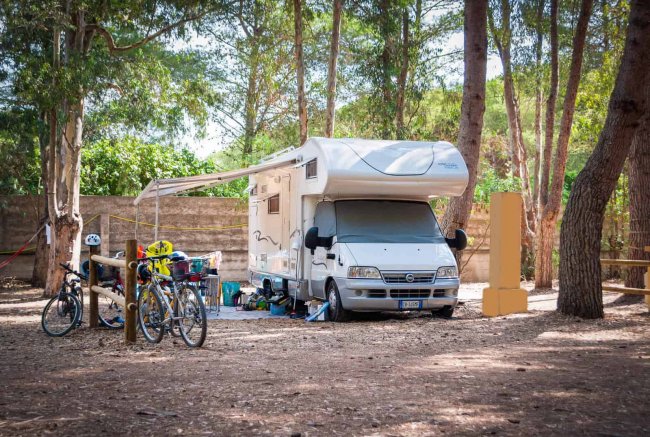 Camper parcheggiato tra gli alberi con biciclette affiancate.