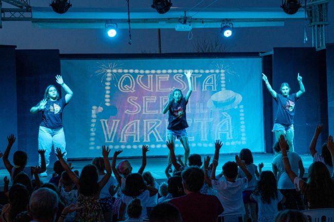 Spettacolo sul palco con bambini davanti.