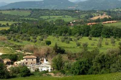 Casale di pietra circondato da alberi e prati collinari.