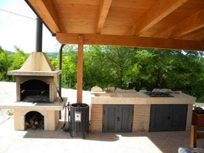 Barbecue e cucina esterna sotto un pergolato con vista verso il verde.