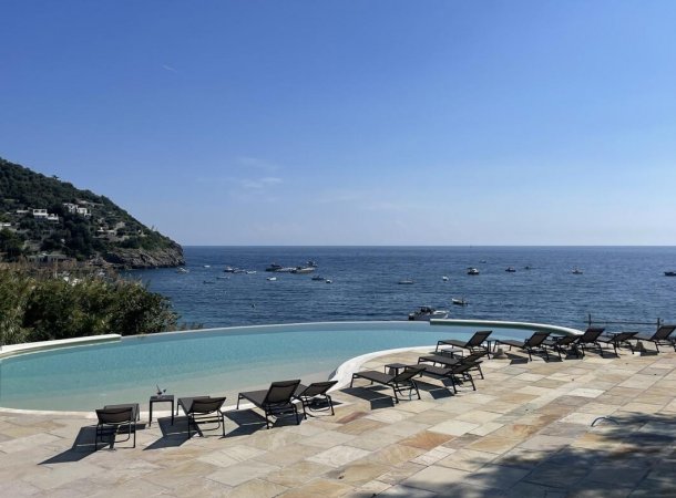 Lettini a bordo piscina con vista sul mare e colline verdi.