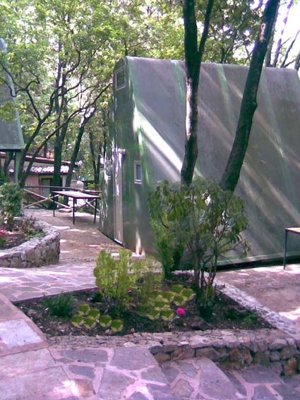 Un prefabbricato verde tra alberi e vialetti in pietra.