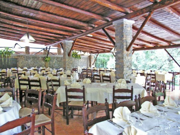 Ampio ristorante all'aperto con tavoli apparecchiati e sedie di legno sotto un tetto rustico.