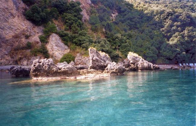 Acqua cristallina e scogliere rocciose con vegetazione lussureggiante sullo sfondo.