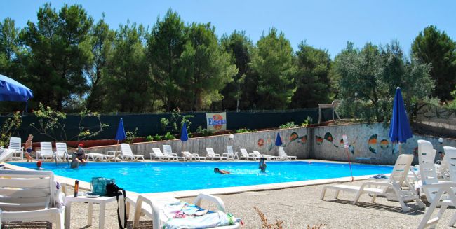Una piscina con lettini e ombrelloni vicino ad alberi.