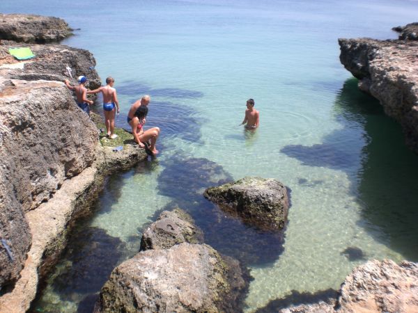 Bambini giocano e nuotano tra rocce vicino al mare trasparente.