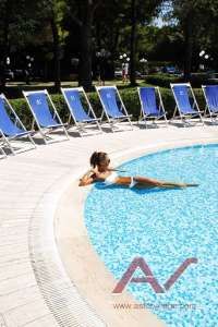 Piscina circondata da sdraio blu, persona in costume bianco si rilassa sul bordo.