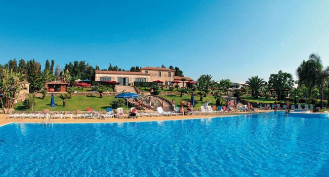 Piscina grande con sdraio e vegetazione circostante.