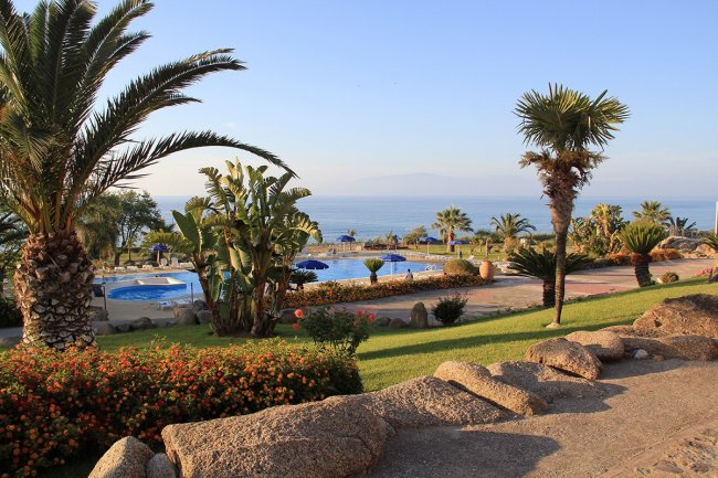 Vista sul mare con piscina e palme in primo piano.
