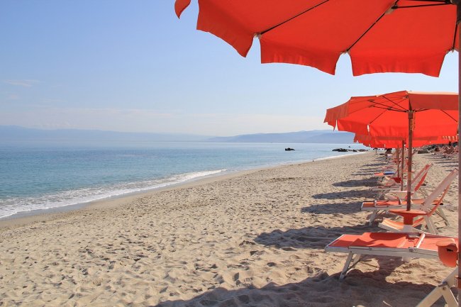 Spiaggia sabbiosa con ombrelloni arancioni.