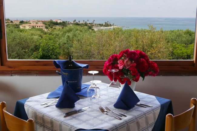Tavolo elegante con vista mare e fiori rossi.