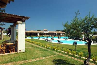 Tavoli e sedie sotto una pergola vicino a una piscina. Area verde ben curata.