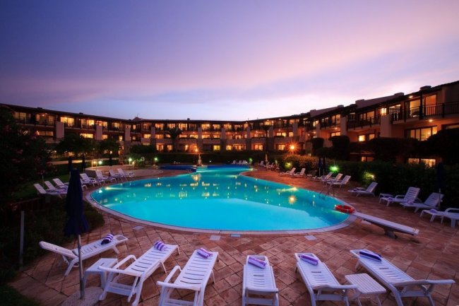 Piscina illuminata al tramonto con sdraio attorno.