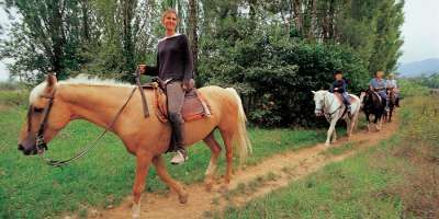 Tre persone a cavallo camminano lungo un sentiero in un ambiente boscoso.