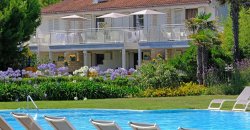 Piscina con sedie a sdraio, giardino fiorito e edificio con balconi sullo sfondo.