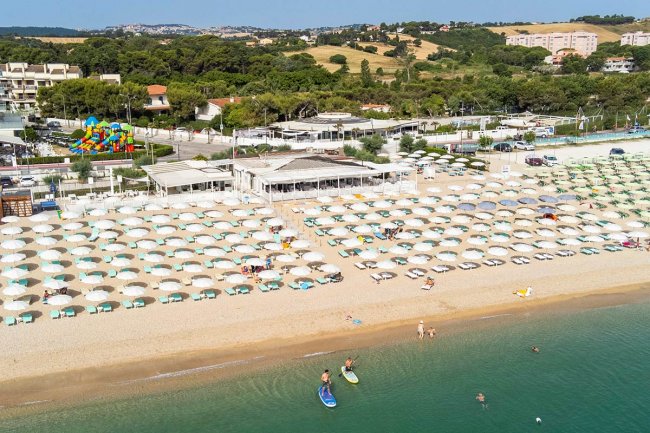 Spiaggia con ombrelloni, mare calmo e persone su tavole da surf.