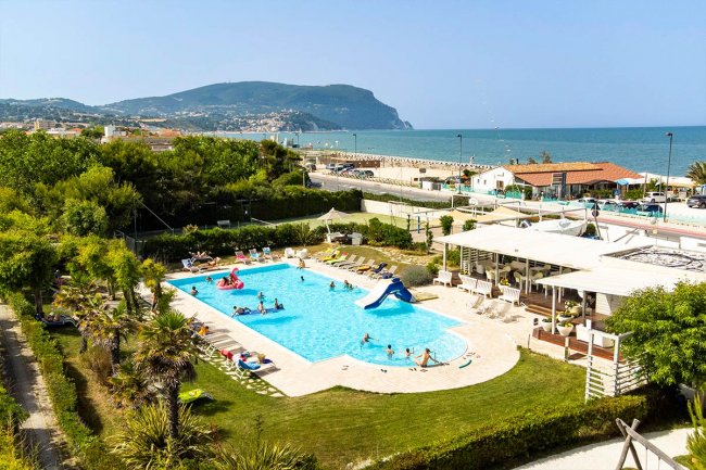 Piscina all'aperto con persone, vicino alla spiaggia e vista montagna.