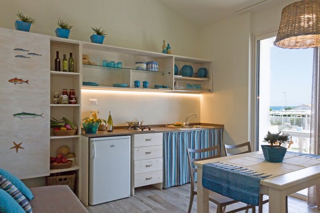 Cucina luminosa con frigorifero, mensole e tavolo, decorata in blu e bianco con un tocco marino.