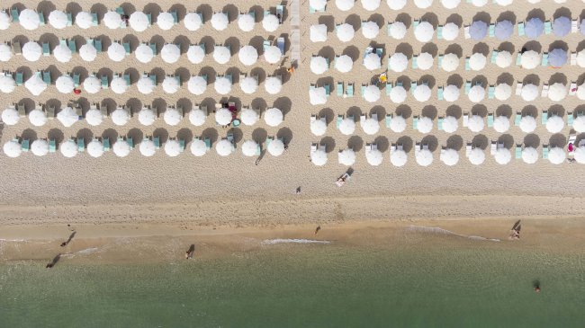 Spiaggia con file ordinate di ombrelloni bianchi.