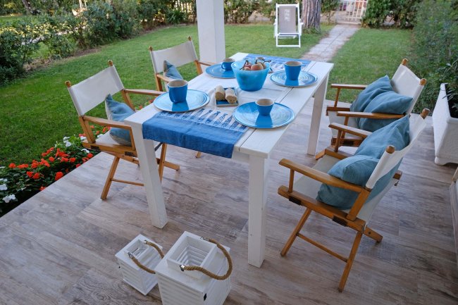 Tavolo da pranzo all'aperto con stoviglie blu e sedie in legno, su una terrazza con giardino.
