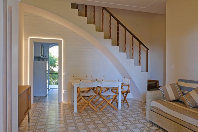 Interno di una casa con scala a chiocciola, tavolo da pranzo e divano con cuscini.