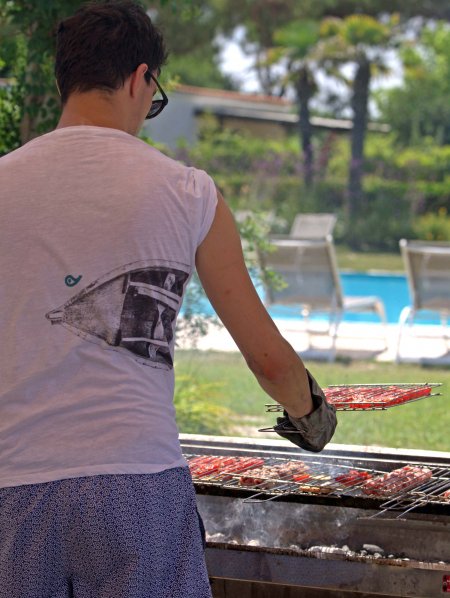 Una persona in maglietta e pantaloncini cucina alla griglia vicino a una piscina.