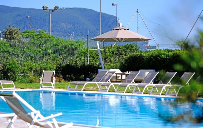 Una piscina con lettini e un ombrellone, circondata da vegetazione e montagne.