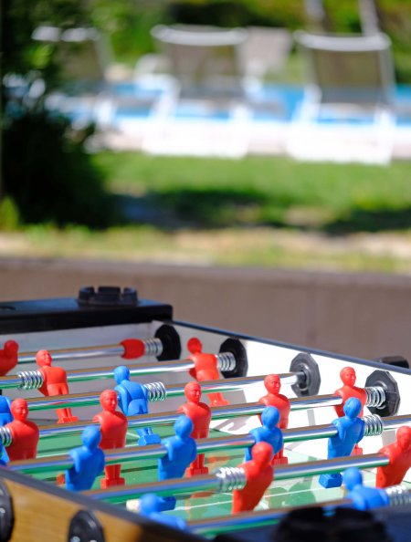 Calcetto da tavolo con giocatori rossi e blu, sfondo piscina sfocato.