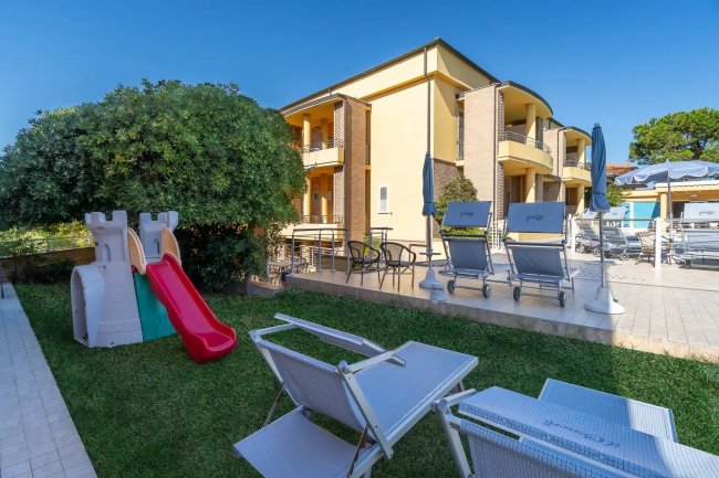 Giardino con sdraio, scivolo rosso e edificio giallo.