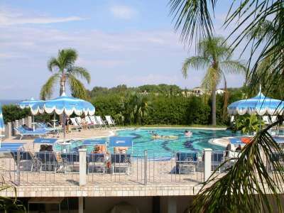 Piscina circondata da palme e lettini con ombrelloni blu.