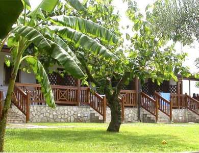 Vista su bungalow in pietra e legno, con un albero di banane e prato verde davanti.