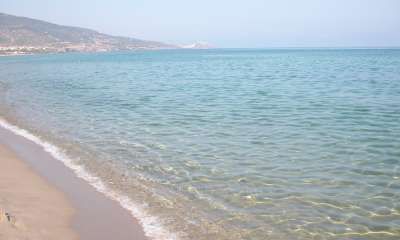 Una spiaggia con una distesa di sabbia dorata e mare calmo, montagne in lontananza.