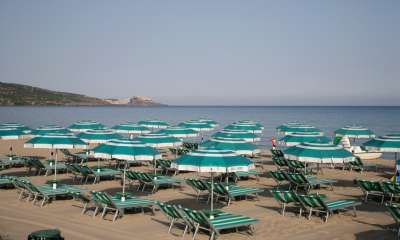 Ombrelloni verde acqua su una spiaggia sabbiosa con mare calmo sullo sfondo.
