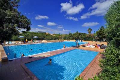 Grande piscina all'aperto con persone che nuotano e si rilassano sotto il cielo blu.