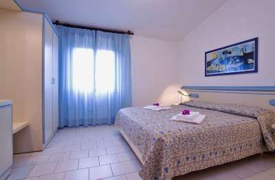 Camera con letto matrimoniale, tendaggi azzurri e quadro sul muro.